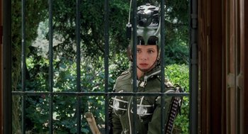 Movie still from “Kika” (1993), directed by Pedro Almodóvar – A woman in a green jacket standing behind a metal fence; Close Up shot, Over the shoulder angle