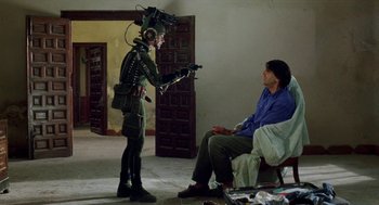 Movie still from “Kika” (1993), directed by Pedro Almodóvar – A man sitting on a chair in front of another man; Wide shot, Over the shoulder angle