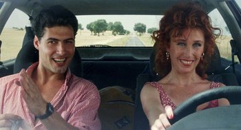 Movie still from “Kika” (1993), directed by Pedro Almodóvar – A man and a woman sitting in the drivers seat of a car; Medium shot, Low angle