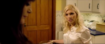 Movie still from “Kill List” (2011), directed by Ben Wheatley – A woman standing in front of a stove in a kitchen; Medium shot, Over the shoulder angle