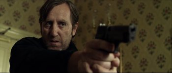 Movie still from “Kill List” (2011), directed by Ben Wheatley – A man holding a gun in a room; Close Up shot, Over the shoulder angle