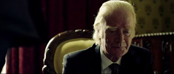 Movie still from “Kill List” (2011), directed by Ben Wheatley – An older man in a suit and tie sitting in a chair; Close Up shot, Over the shoulder angle