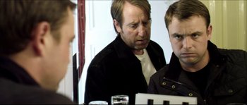 Movie still from “Kill List” (2011), directed by Ben Wheatley – A man in a black jacket is looking at his reflection in a mirror; Medium shot, Over the shoulder angle