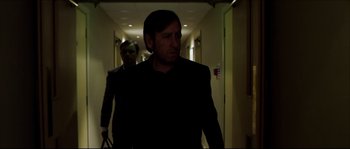 Movie still from “Kill List” (2011), directed by Ben Wheatley – A man in a black suit walking down a hall way; Medium shot, Over the shoulder angle