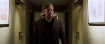 Movie still from “Kill List” (2011), directed by Ben Wheatley – A man in a suit walking down a hall way; Medium shot, Over the shoulder angle