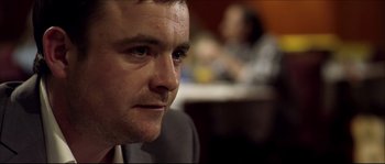 Movie still from “Kill List” (2011), directed by Ben Wheatley – A person wearing a suit; Close Up shot, Over the shoulder angle