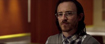 Movie still from “Kill List” (2011), directed by Ben Wheatley – A person wearing glasses and a vest; Close Up shot, Over the shoulder angle