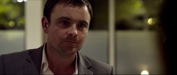 Movie still from “Kill List” (2011), directed by Ben Wheatley – A person wearing a suit and tie; Close Up shot, Over the shoulder angle