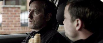 Movie still from “Kill List” (2011), directed by Ben Wheatley – A man sitting in the back seat of a car; Close Up shot, Over the shoulder angle