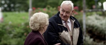 Movie still from “Kill List” (2011), directed by Ben Wheatley – An older man and a woman talking to each other; Medium shot, Over the shoulder angle