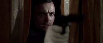 Movie still from “Kill List” (2011), directed by Ben Wheatley – A person holding a gun in a room; Close Up shot, Over the shoulder angle