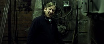 Movie still from “Kill List” (2011), directed by Ben Wheatley – A man standing in front of a wall with electrical wires; Medium shot, Low angle