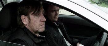 Movie still from “Kill List” (2011), directed by Ben Wheatley – Two men sitting in the drivers seat of a car; Medium shot, Over the shoulder angle