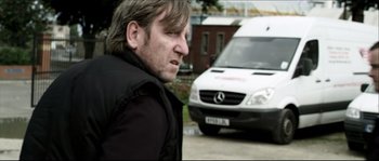 Movie still from “Kill List” (2011), directed by Ben Wheatley – A person in a parking lot near a van; Medium shot, Over the shoulder angle