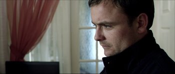 Movie still from “Kill List” (2011), directed by Ben Wheatley – A person wearing a black jacket; Close Up shot, Over the shoulder angle