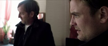 Movie still from “Kill List” (2011), directed by Ben Wheatley – A man in a black jacket is looking at another man in a black jacket; Close Up shot, Over the shoulder angle