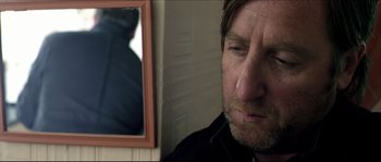 Movie still from “Kill List” (2011), directed by Ben Wheatley – A person looking at a mirror; Close Up shot, Over the shoulder angle