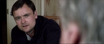 Movie still from “Kill List” (2011), directed by Ben Wheatley – A person sitting at a table; Close Up shot, Over the shoulder angle