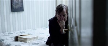 Movie still from “Kill List” (2011), directed by Ben Wheatley – An older man leaning against a wall with his hand to his mouth; Medium shot, High angle