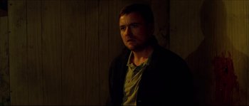 Movie still from “Kill List” (2011), directed by Ben Wheatley – A man standing in the dark in a room; Close Up shot, Over the shoulder angle