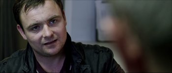 Movie still from “Kill List” (2011), directed by Ben Wheatley – A person wearing a black jacket; Close Up shot, Over the shoulder angle