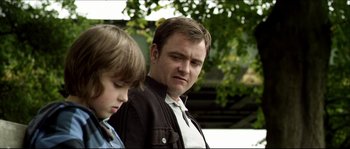 Movie still from “Kill List” (2011), directed by Ben Wheatley – A man standing next to a boy in a park; Close Up shot, Over the shoulder angle