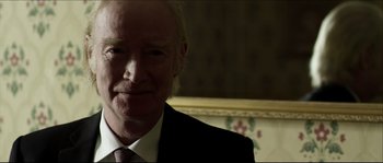 Movie still from “Kill List” (2011), directed by Ben Wheatley – An older man in a suit and tie looking to his left; Close Up shot, Over the shoulder angle