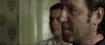 Movie still from “Kill List” (2011), directed by Ben Wheatley – A man with a goatee and a beard looking into the distance; Close Up shot, Over the shoulder angle