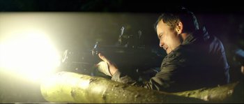 Movie still from “Kill List” (2011), directed by Ben Wheatley – A man sitting in the dark holding a gun; Medium shot, Low angle