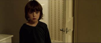 Movie still from “Kill List” (2011), directed by Ben Wheatley – A young boy standing in front of an open door; Close Up shot, High angle