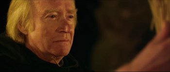 Movie still from “Kill List” (2011), directed by Ben Wheatley – An older man looking at the camera in a dimly - lit room; Close Up shot, Over the shoulder angle