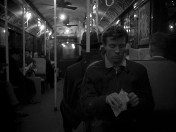 Movie still from “Killer's Kiss” (1955), directed by Stanley Kubrick – A man standing on a train holding papers; Medium shot, High angle