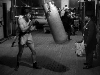 Movie still from “Killer's Kiss” (1955), directed by Stanley Kubrick – A man in a boxing ring holding a punching bag; Wide shot, High angle