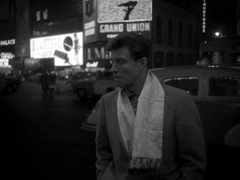 Movie still from “Killer's Kiss” (1955), directed by Stanley Kubrick – A black and white photo of a man wearing a suit and a scarf; Medium shot, Low angle