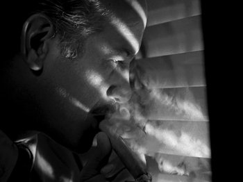 Movie still from “Killer's Kiss” (1955), directed by Stanley Kubrick – A black and white photo of a man smoking a cigarette; Close Up shot, Low angle