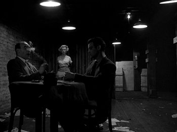 Movie still from “Killer's Kiss” (1955), directed by Stanley Kubrick – A man sitting at a table in front of two women; Wide shot, Over the shoulder angle