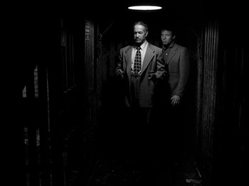 Movie still from “Killer's Kiss” (1955), directed by Stanley Kubrick – A couple of men standing next to each other in a dark room; Medium shot, Low angle