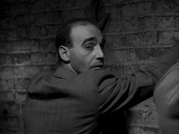 Movie still from “Killer's Kiss” (1955), directed by Stanley Kubrick – Black and white photograph of a man leaning against a brick wall; Medium shot, Low angle