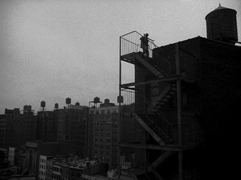 Movie still from “Killer's Kiss” (1955), directed by Stanley Kubrick – A man standing on top of a fire escape on top of a building; Extreme Wide shot, Low angle