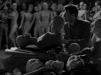 Movie still from “Killer's Kiss” (1955), directed by Stanley Kubrick – A group of mannequins in a room next to a man and a woman; Wide shot, High angle