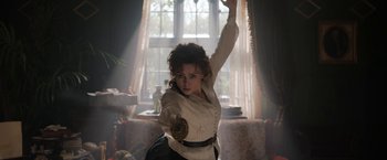 Movie still from “Enola Holmes” (2020), directed by Harry Bradbeer – A woman in white shirt and black skirt holding a sword in a living room; Medium shot, Low angle