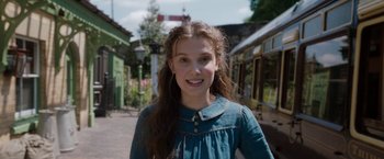 Movie still from “Enola Holmes” (2020), directed by Harry Bradbeer – A young woman standing on the side of the street; Close Up shot, Over the shoulder angle