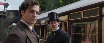 Movie still from “Enola Holmes” (2020), directed by Harry Bradbeer – Two men standing next to each other in front of a train; Close Up shot, Over the shoulder angle