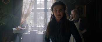 Movie still from “Enola Holmes” (2020), directed by Harry Bradbeer – A woman in a green dress standing in front of a window; Medium shot, Over the shoulder angle