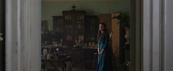 Movie still from “Enola Holmes” (2020), directed by Harry Bradbeer – A woman standing in front of a bookshelf in a living room; Wide shot, Low angle