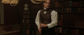 Movie still from “Enola Holmes” (2020), directed by Harry Bradbeer – A man in a vest holding a cane in a library; Medium shot, Over the shoulder angle