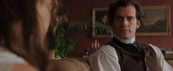 Movie still from “Enola Holmes” (2020), directed by Harry Bradbeer – A man sitting on top of a couch in a living room; Close Up shot, Over the shoulder angle