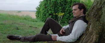 Movie still from “Enola Holmes” (2020), directed by Harry Bradbeer – A man sitting on the ground holding a cell phone; Medium shot, High angle