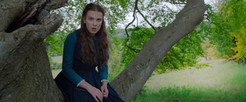 Movie still from “Enola Holmes” (2020), directed by Harry Bradbeer – A young woman leaning up against a tree branch; Medium shot, Low angle