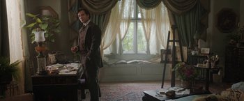 Movie still from “Enola Holmes” (2020), directed by Harry Bradbeer – A man standing in front of an easel in front of a window; Wide shot, High angle